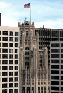 The historic Chicago Tribune Tower stands tall between modern office buildings, with its neo-Gothic architecture and an American flag waving above. The image symbolizes the legacy and forward momentum of the Chicago Tribune as it expands its “Dream Partnership” initiative to uplift and inspire local communities.
