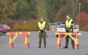 Two uniformed officers stand guard behind road barricades in a wooded area, maintaining a secured perimeter, following a deadly incident where a game warden shot and killed a man who attacked with a knife in Middle Georgia, according to the GBI.